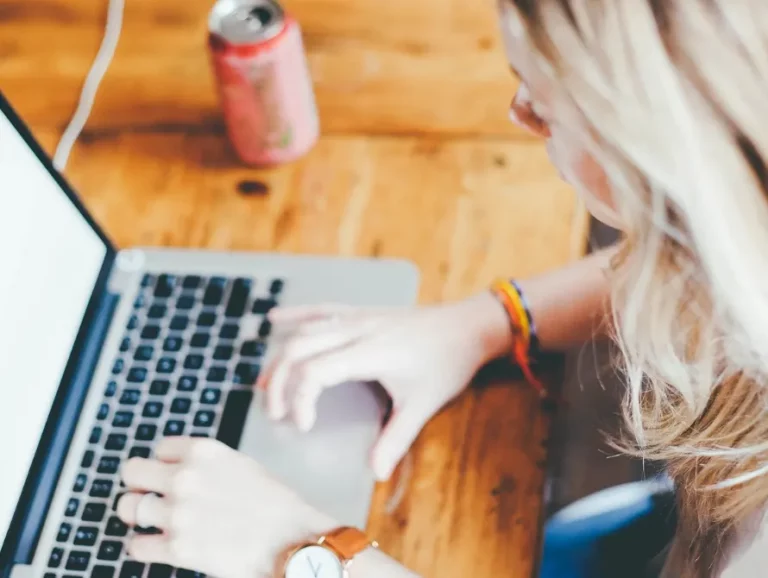Eine junge blonde Frau tippt auf ihrem Laptop.